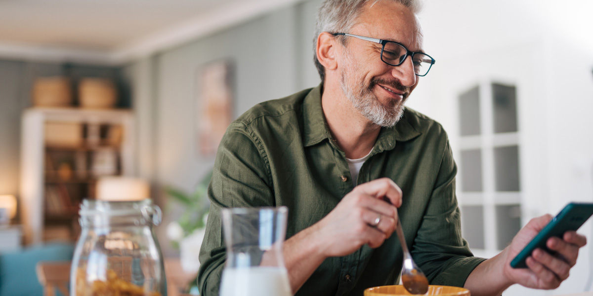 Man eating breakfast, using mobile phone.